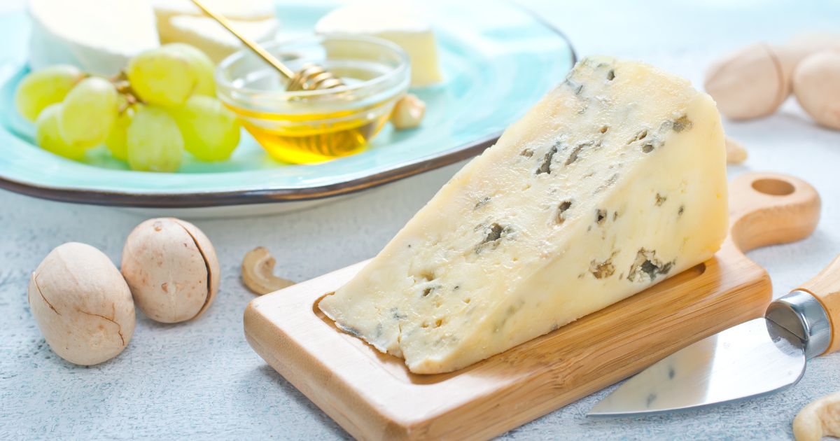 Cuña de queso azul sobre tabla de cortar de madera rústica con cuchillo para queso.