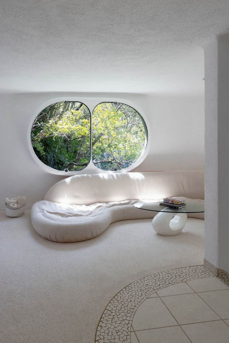 Sala de estar de la casa de serpientes con un sofá blanco curvo debajo de una gran ventana ovalada