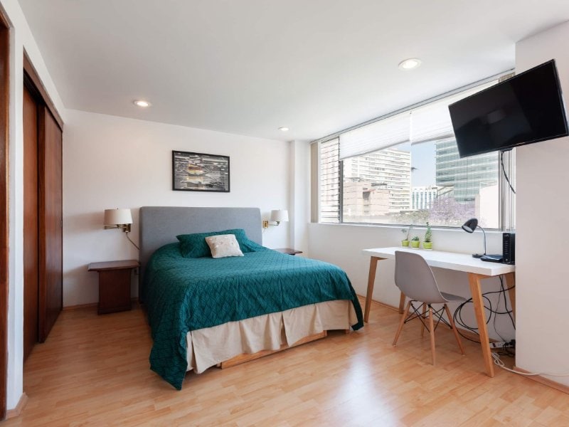 Cama tamaño queen con funda verde y escritorio junto a la ventana en Bright Studio en Nápoles, Ciudad de México