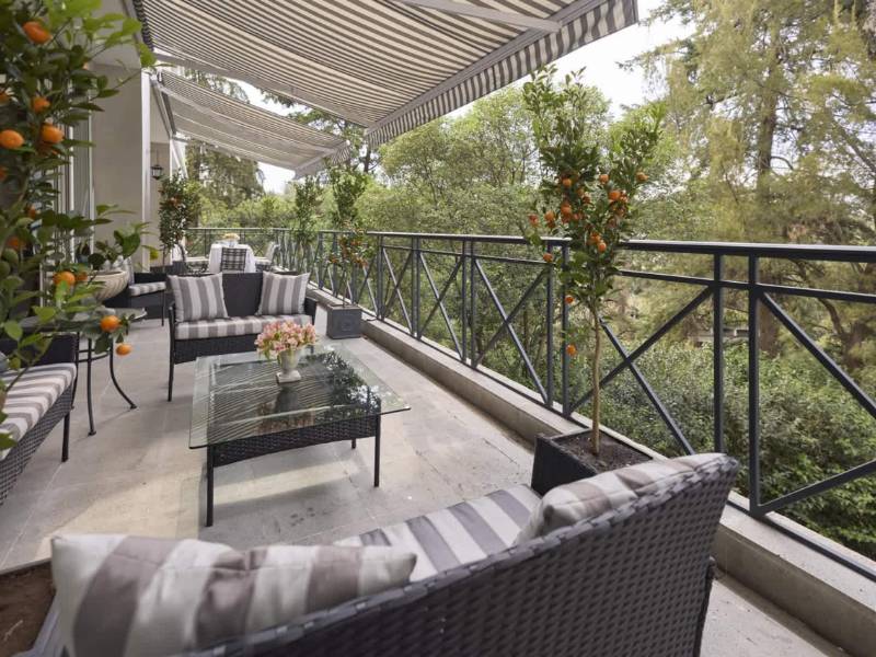 Terraza cubierta con sofás rodeada de árboles en la Villa de Lujo en Lomas Altas, Ciudad de México