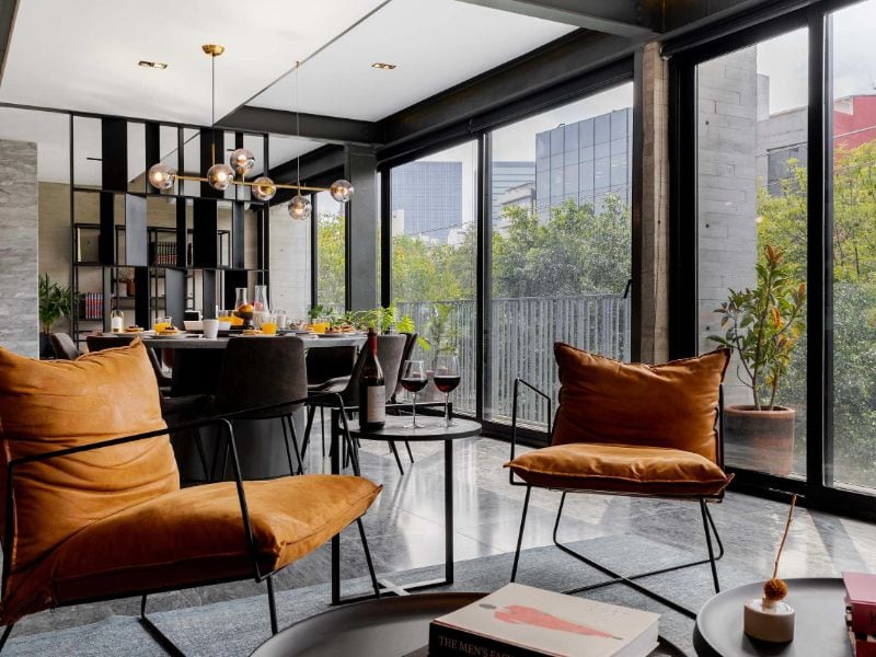 Sala de estar con paredes de vidrio y sillones naranjas en el Apartamento Polanco de 3 dormitorios de Masaryk, un Airbnb de lujo en Ciudad de México