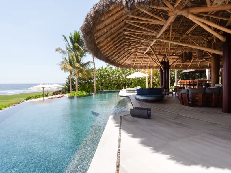 Piscina infinita debajo de una palapa con techo de palma frente al mar en Casa Koko en Punta Mita