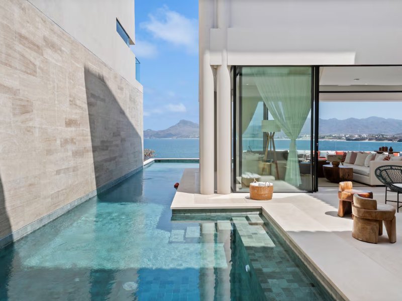 Piscina junto a paredes de vidrio y fachada de piedra en Casa Dinamita, una villa de Kupuri Punta Mita