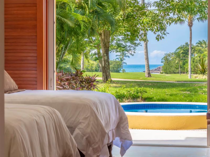 Dormitorio con vista al jardín, la piscina y el océano en una villa con vista al mar en Punta Mita en Las Palmas