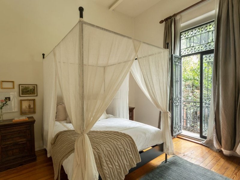 Cama con dosel junto a las puertas del balcón en la antigua casa del siglo XX Airbnb en Roma Norte, Ciudad de México